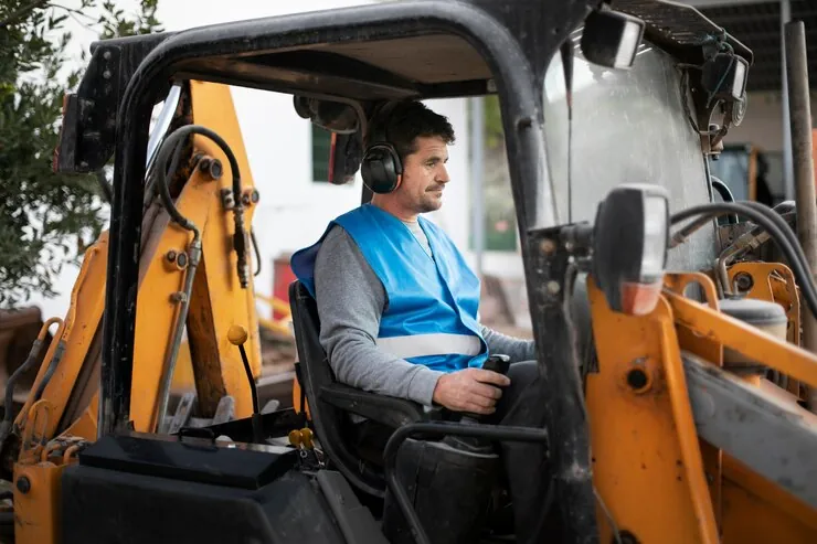 Operator cu antifoane la comenzile unui buldoexcavator